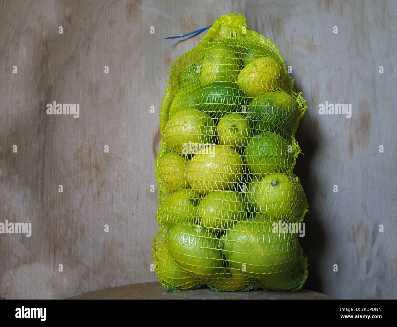 Un sacco a rete di limoni su fondo astratto in legno. Foto Stock