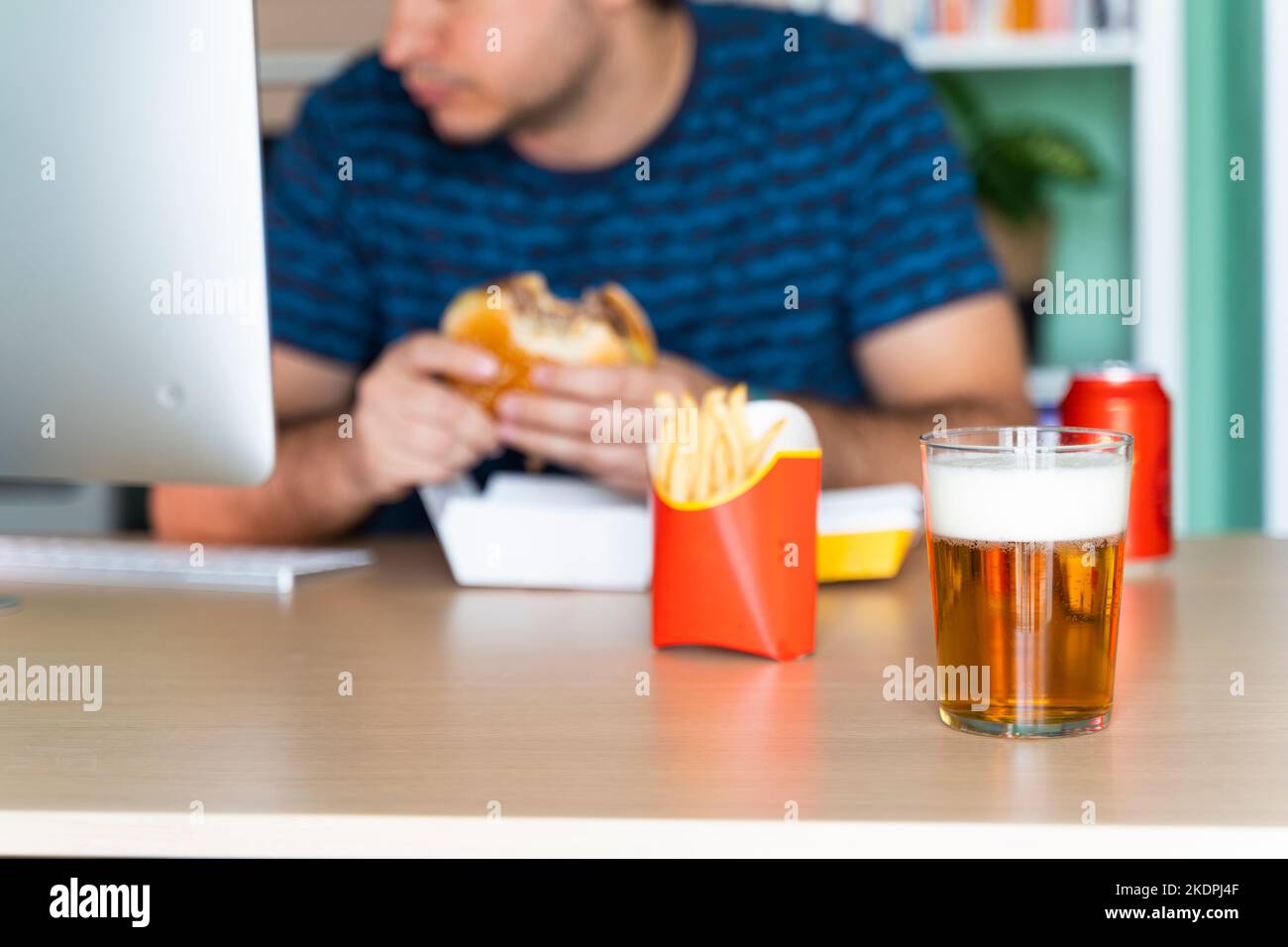 Uomo che mangia fast food mentre lavora nel suo ufficio di fronte al computer Foto Stock