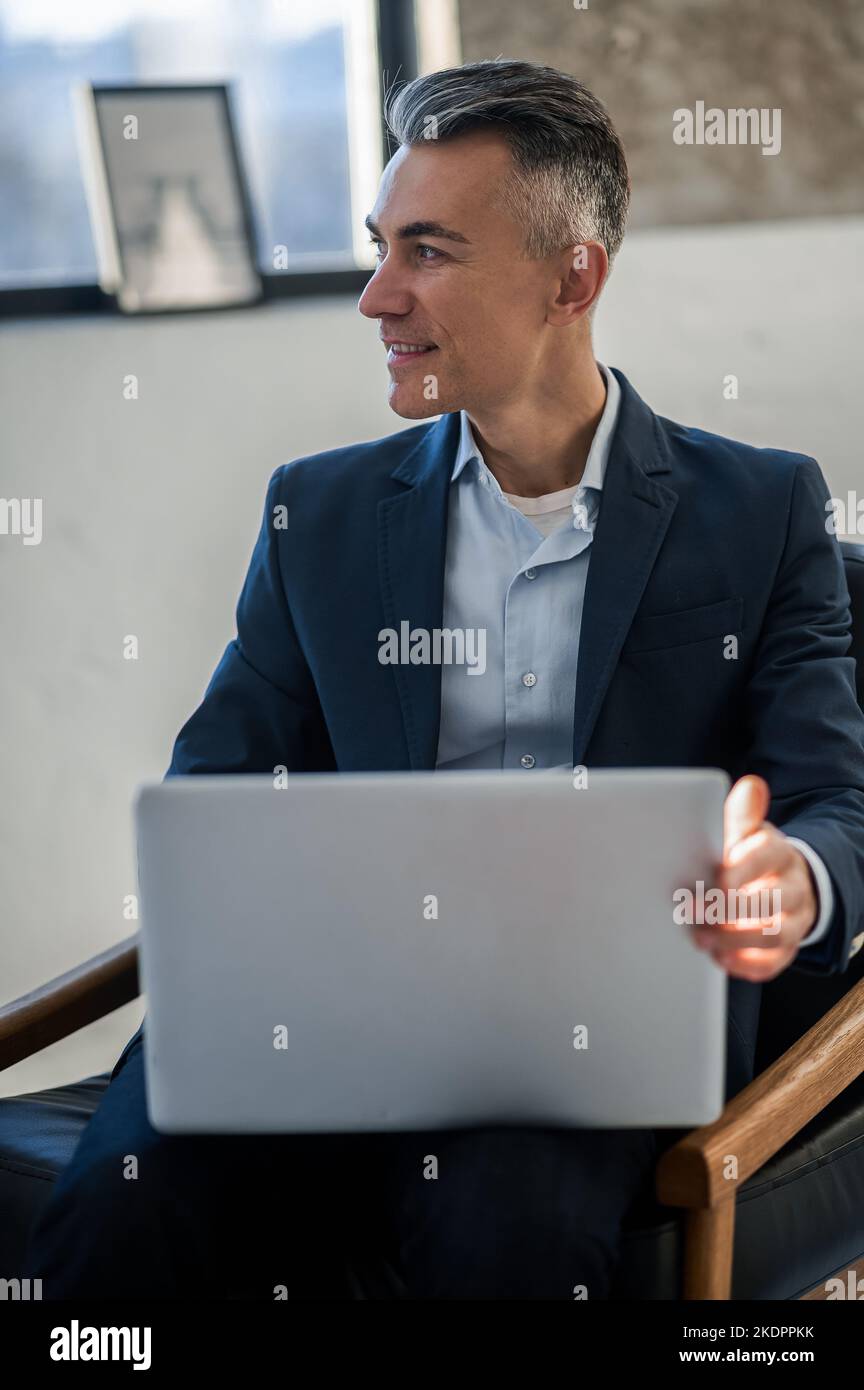 Uomo elegante e dall'aspetto elegante in tuta che lavora su un computer portatile Foto Stock