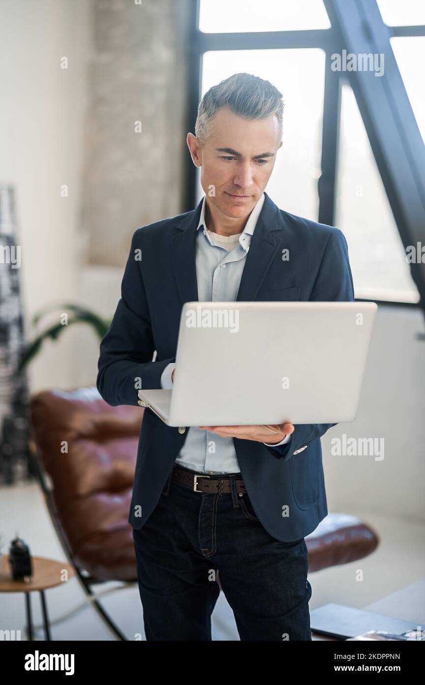 Uomo elegante e dall'aspetto elegante in tuta che lavora su un computer portatile Foto Stock