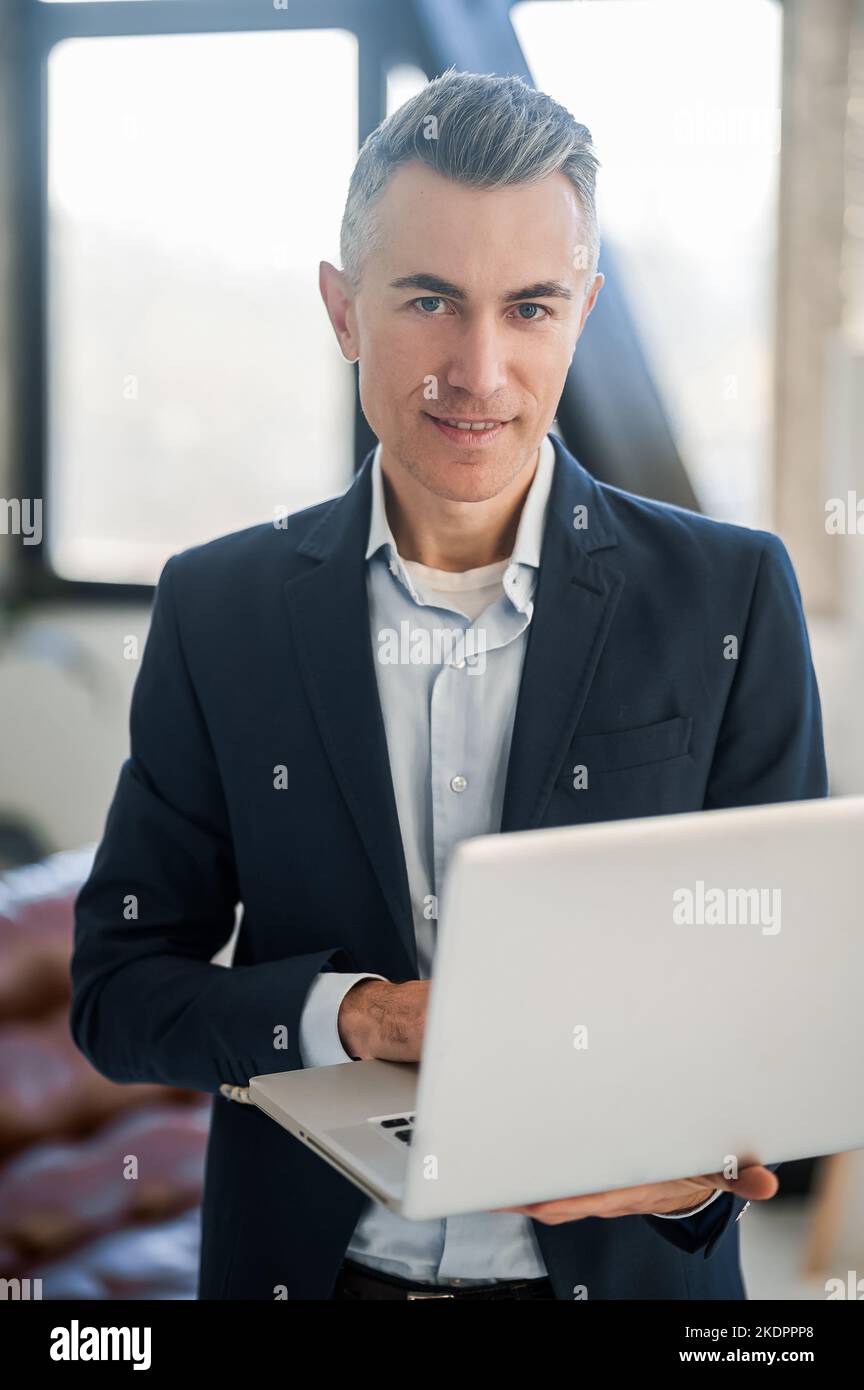 Uomo elegante e dall'aspetto elegante in tuta che lavora su un computer portatile Foto Stock