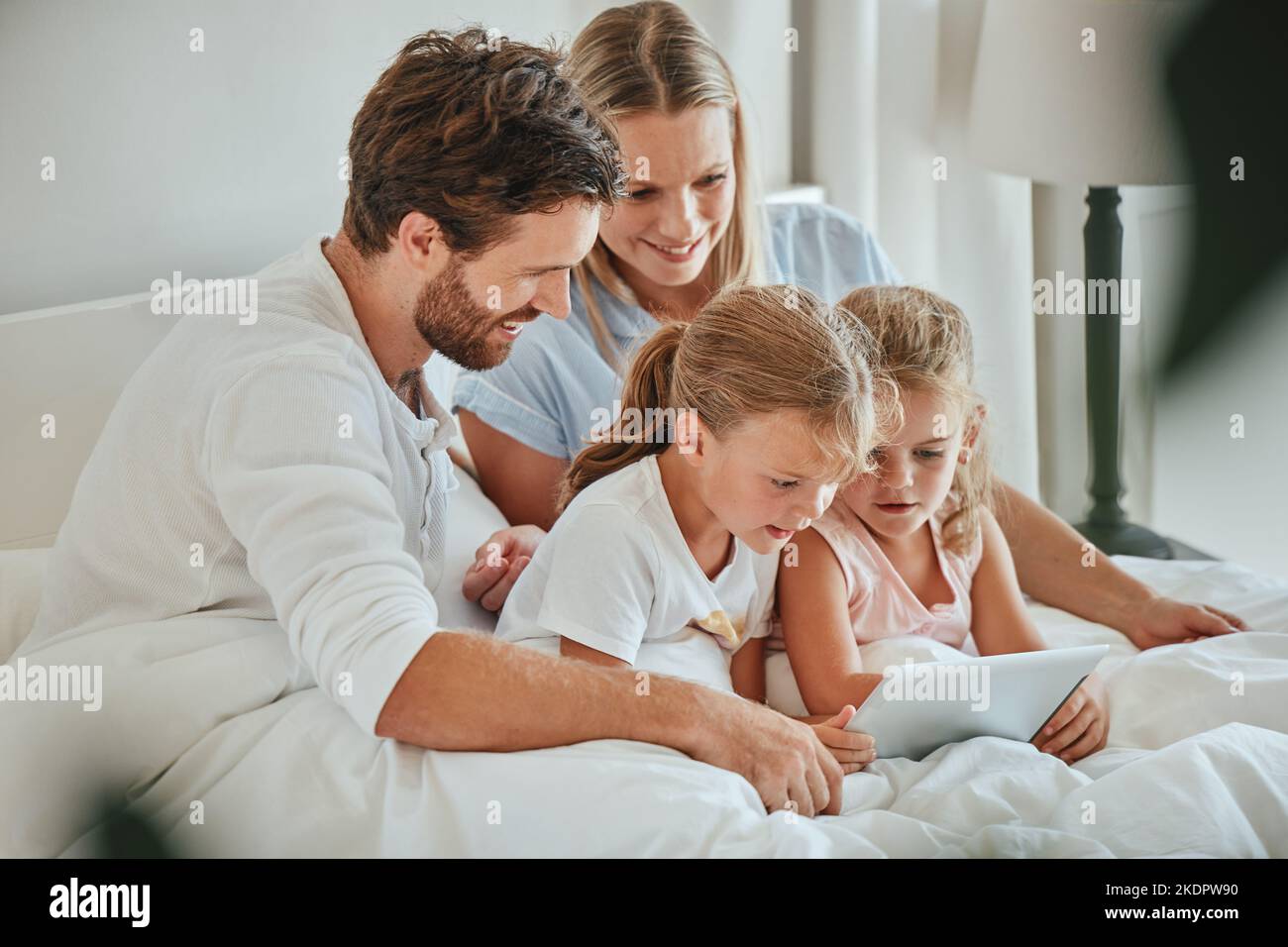 Felice, famiglia e tablet per l'intrattenimento a letto guardando gli spettacoli insieme mentre si rilassa a casa. Madre, padre e bambini si rilassano con il sorriso per Foto Stock