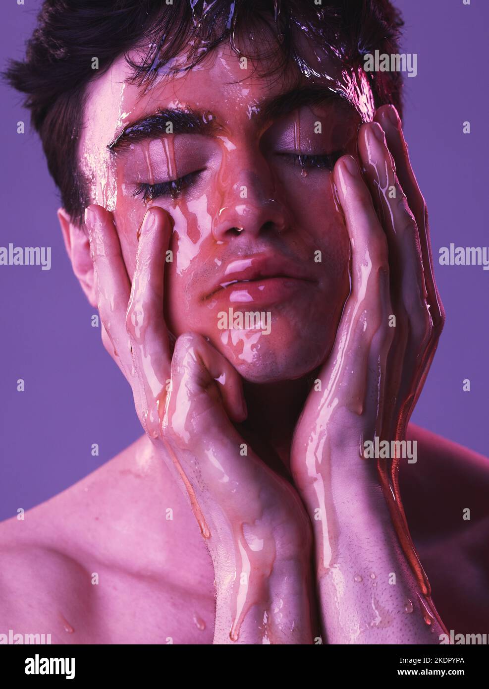 Modella, uomo e cura della pelle con miele che sgocciola sul viso, cosmetici e bellezza biologica da sfondo viola. Pelle, cosmetica e facciale con naturale Foto Stock