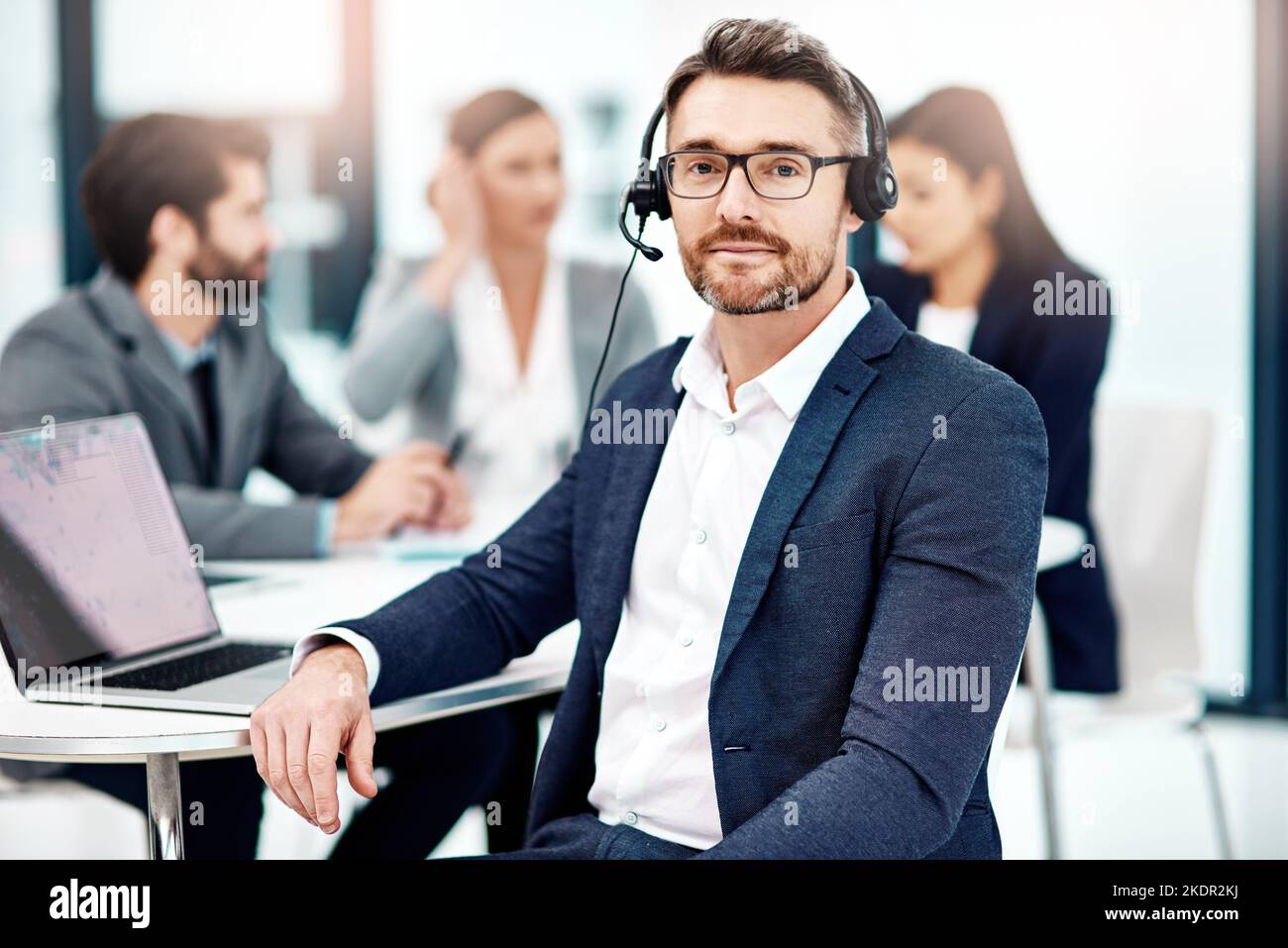 Ricezione di messaggi durante la riunione. Ritratto di un operatore telefonico maschile in ufficio con i suoi colleghi sullo sfondo. Foto Stock