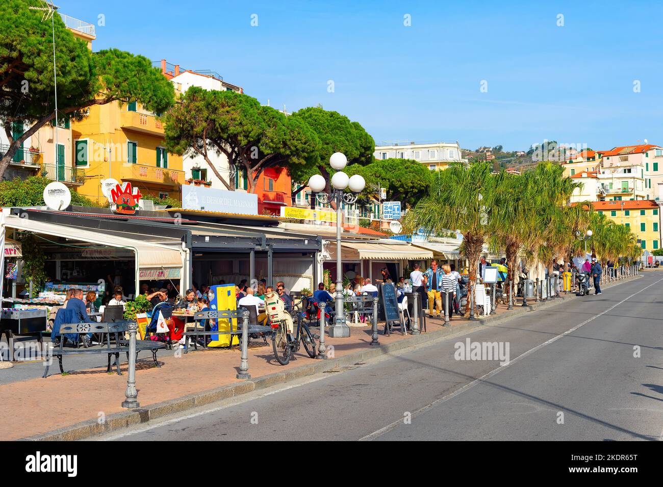 SANREMO, ITALIA - 28 OTTOBRE 2021: Persone che mangiano in ristoranti terrazze di strada in pieno sole, paesaggio urbano con alberi verdi Foto Stock
