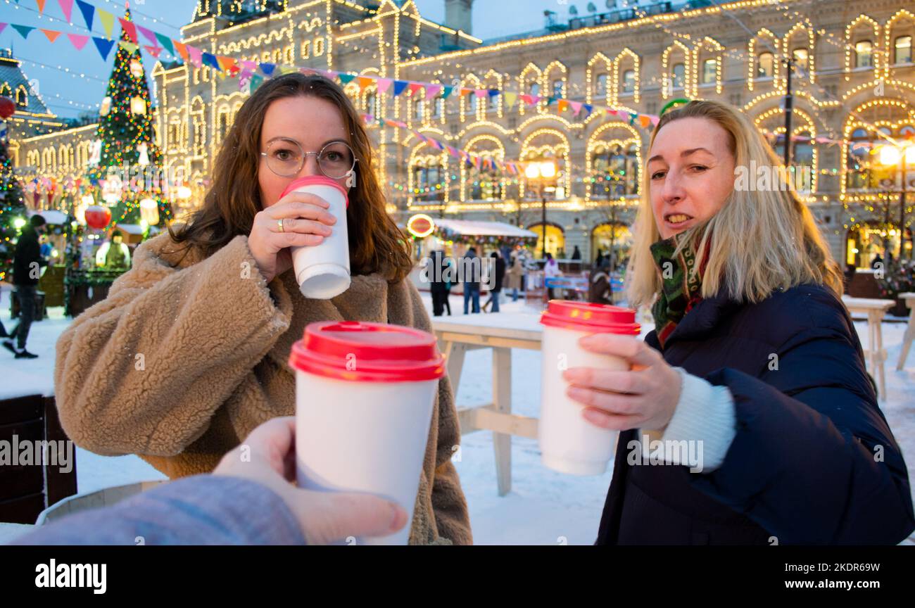 Due giovani donne allegre con coppe di cartone di VIN brulé fanno festa e ridono. Fiera di Natale sulla Piazza Rossa, Mosca. Foto Stock