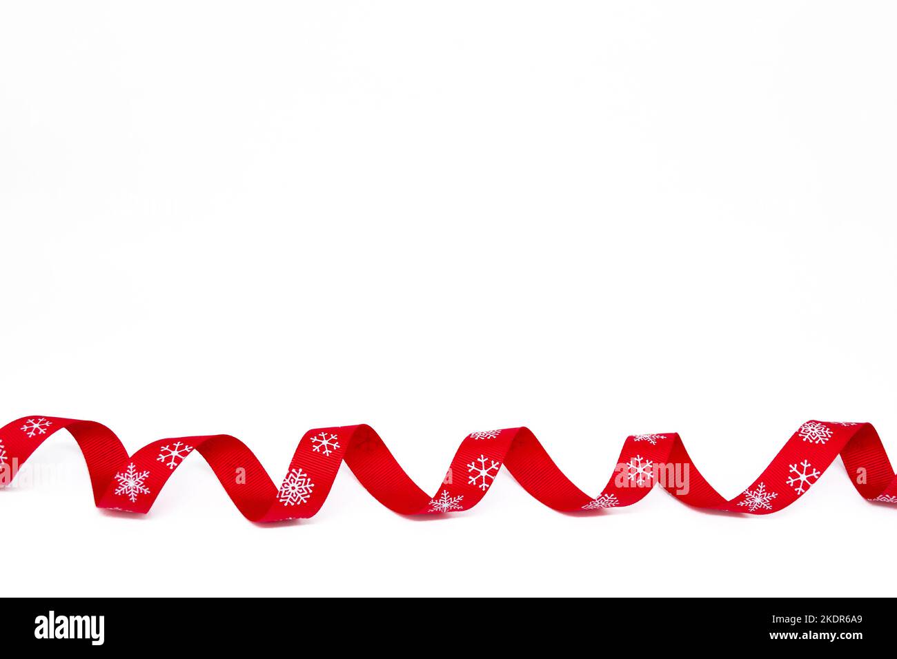 Un nastro rosso riccio luminoso con fiocchi di neve su sfondo bianco. Spazio di copia. Il concetto di Natale, San Valentino e regali. Foto Stock