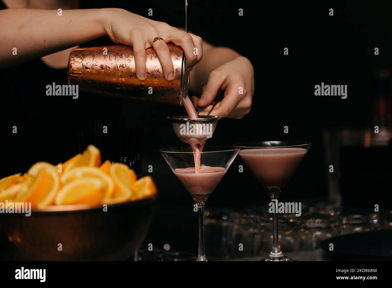 Mixologist che versa cocktail rosa dallo shaker al bicchiere Foto Stock