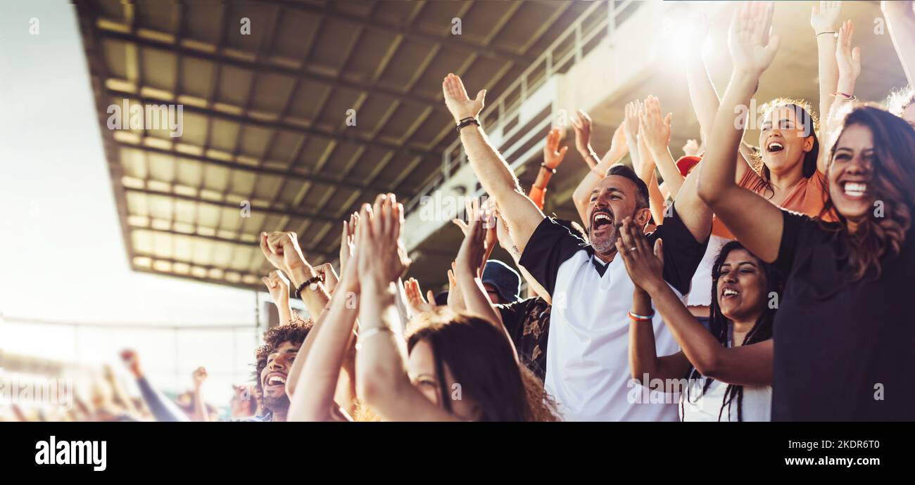 Una folla di tifosi che si tifano per lo sport durante una partita nello stadio. Persone eccitate in piedi con le braccia sollevate, battendo e urlando per incoraggiare la loro squadra Foto Stock