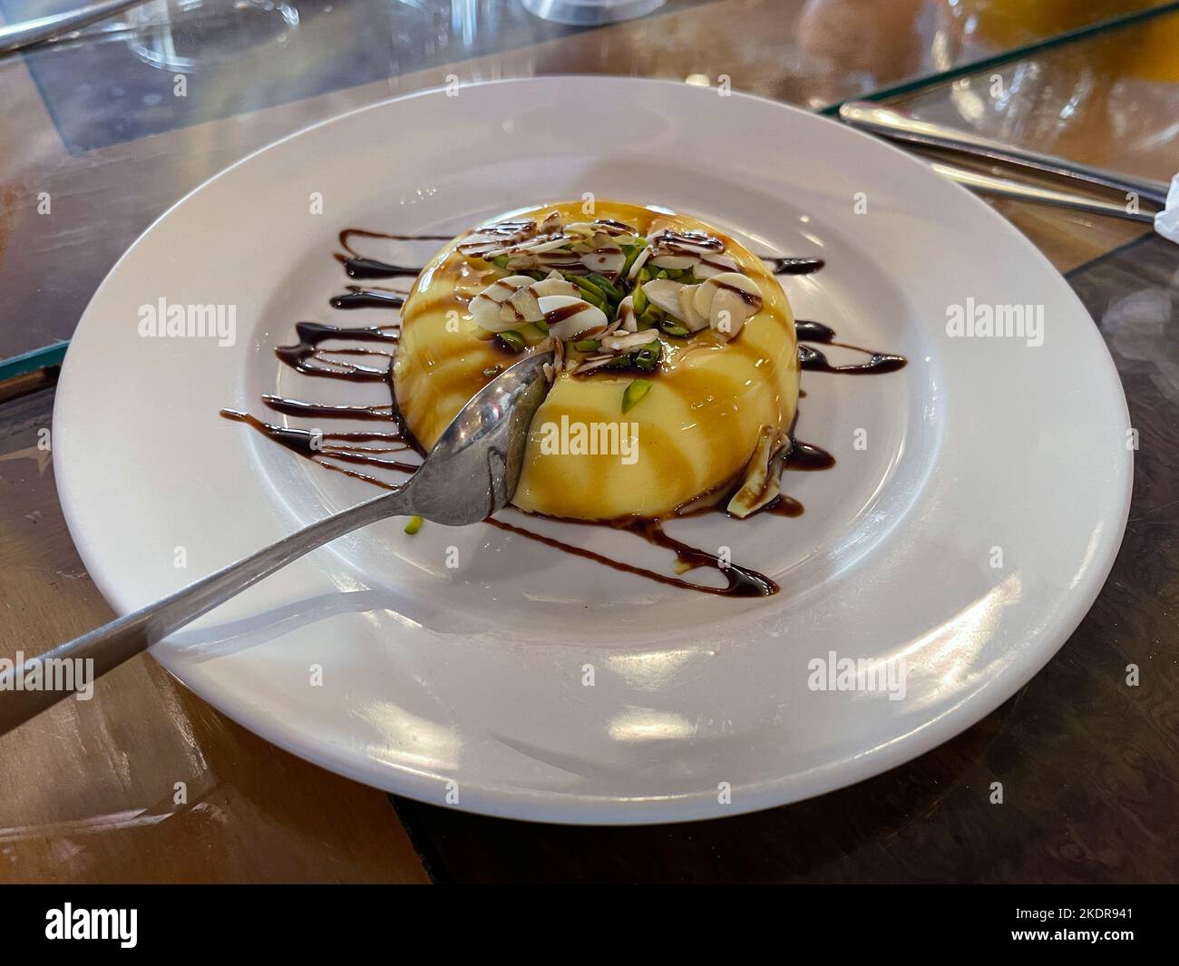 Crema al caramello servita in un piatto bianco con mandorle a fette e pistacchi. Foto Stock