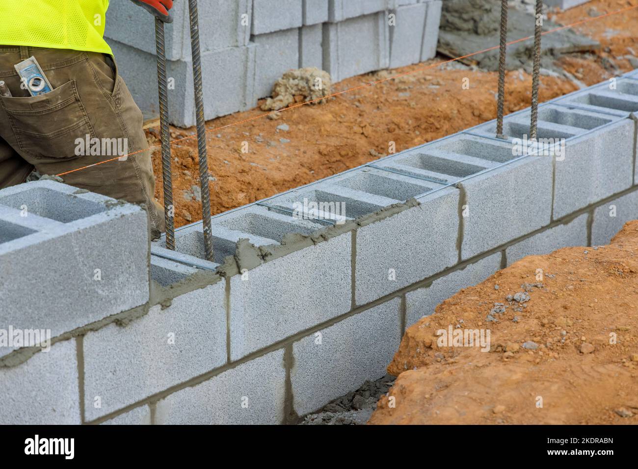 Mettendo giù la seconda fila di blocchi di cemento da muratore lavoratore di costruzione in cantiere Foto Stock