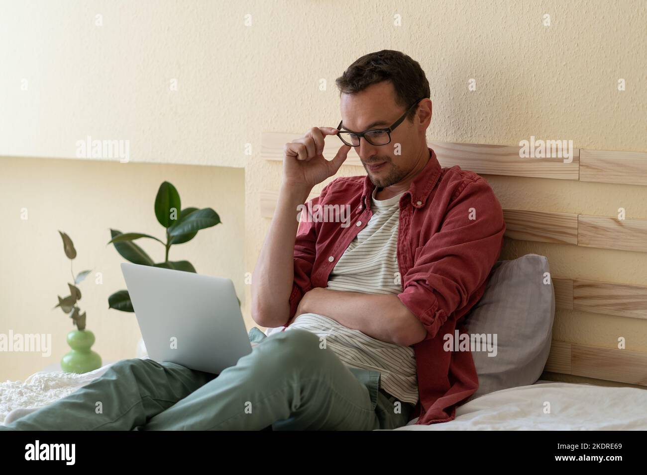 L'uomo caucasico concentrato si siede sul letto nella camera dell'hotel leggendo le notizie via internet o controllando la posta elettronica Foto Stock
