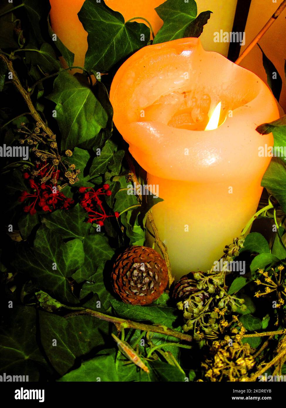 Candela illuminata circondata da foglie e semi come parte di una decorazione di Natale Foto Stock