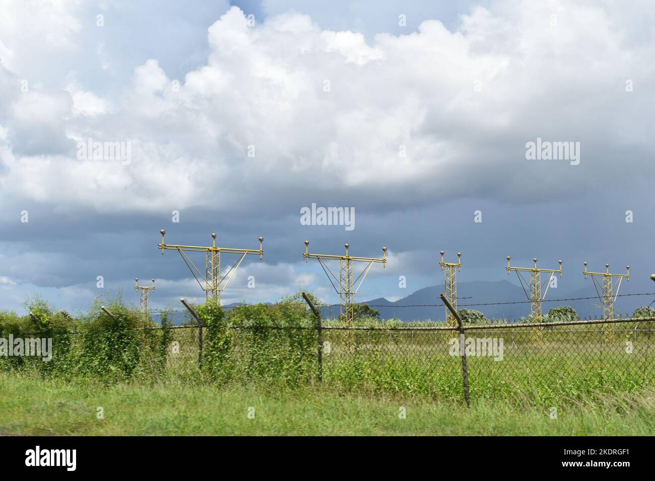 Una serie di strutture di illuminazione di approccio giallo situate dietro una recinzione a catena presso l'aeroporto internazionale di Piarco a Trinidad e Tobago. Foto Stock