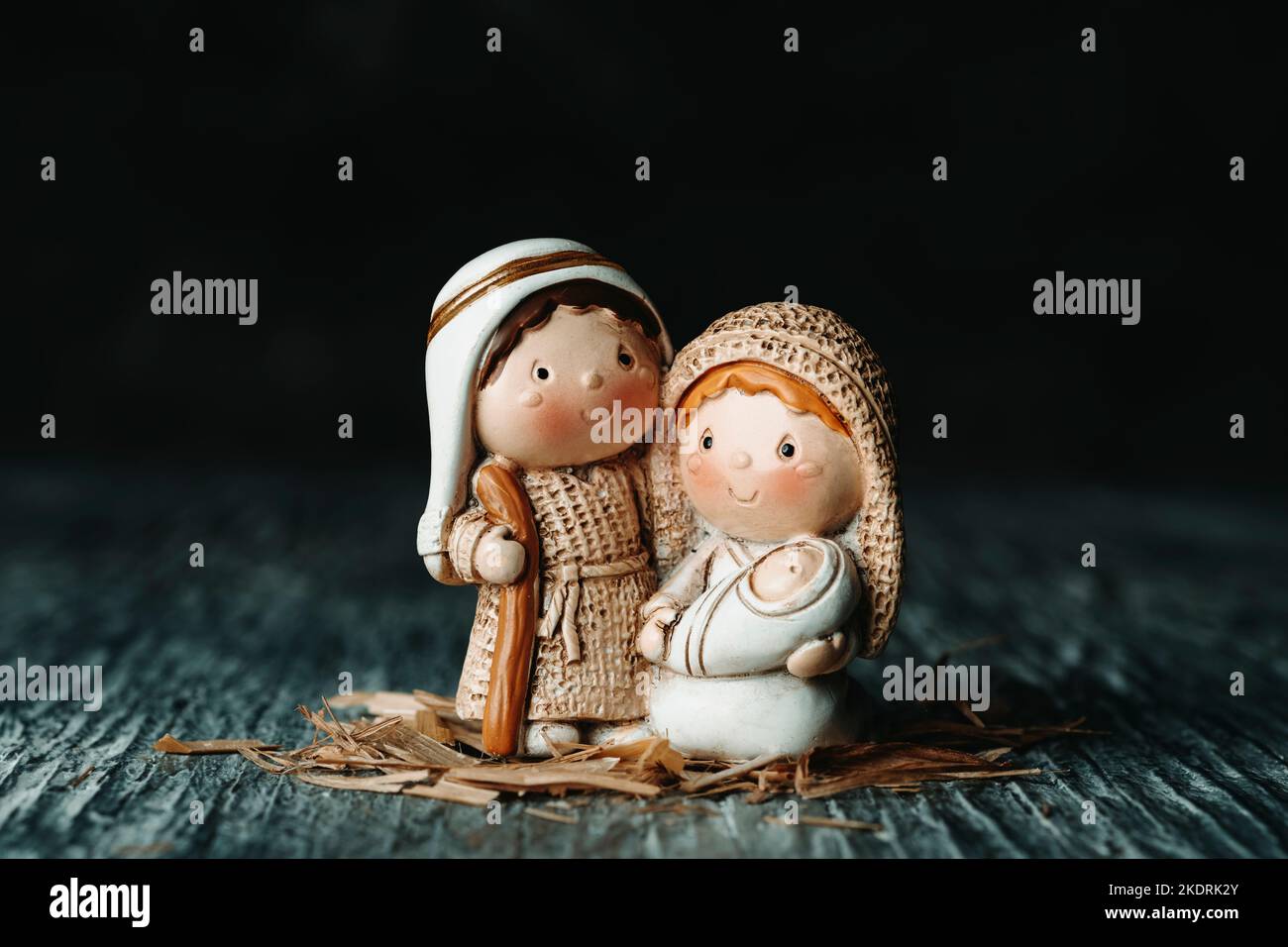 una bella raffigurazione della santa famiglia, san giuseppe e la vergine maria con il bambino gesù in braccio, su una superficie di legno grigio, contro una schiena nera Foto Stock