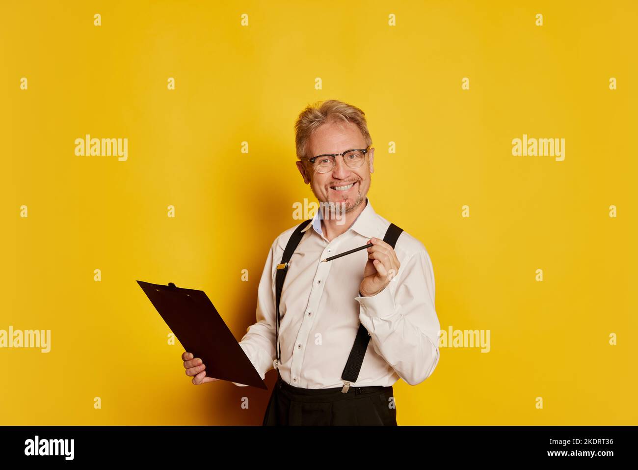 Ritratto dell'uomo maturo in abiti classici di stile in posa isolata su sfondo giallo studio. Professore Foto Stock