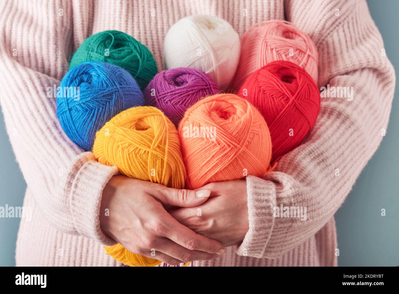 Donna che detiene filati di lana colorati o multicolore su sfondo blu. Molte sfere multicolore di fili primo piano. Concetto di lavorazione a maglia o a cucito. Foto Stock