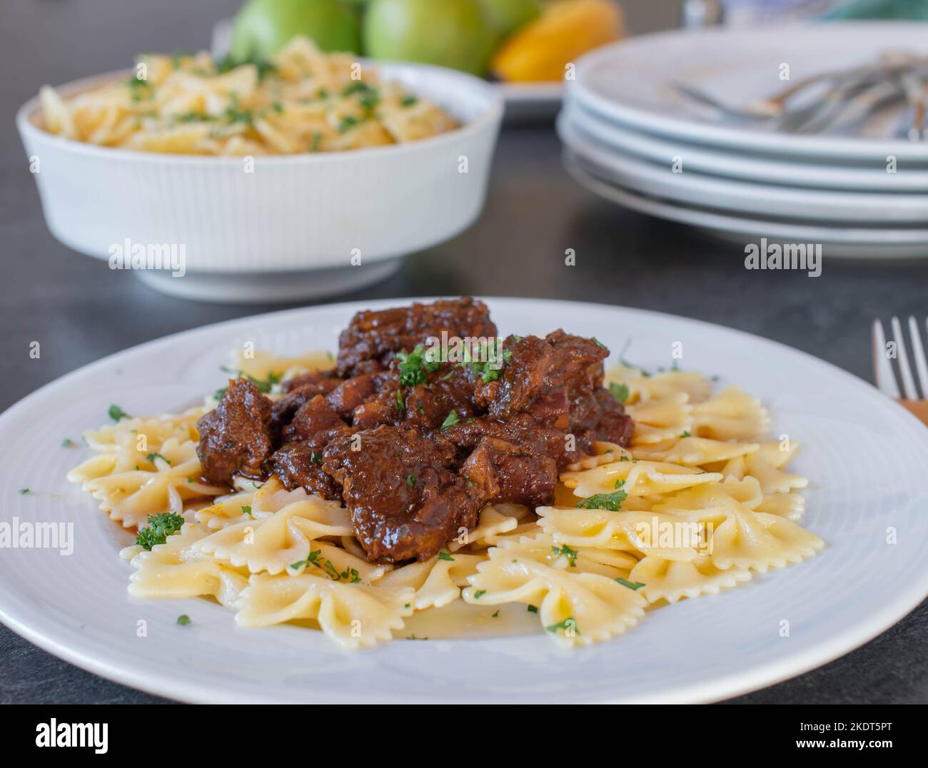 Gulasch di manzo con pasta di farfalle su un piatto sul tavolo da cucina. Vista frontale con sfondo sfocato Foto Stock