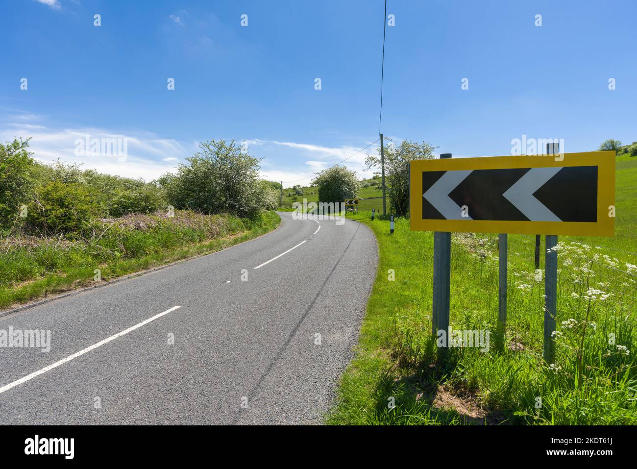 Un segnale di strada bianco e nero che avverte di una curva a sinistra in avvicinamento su Cliff Road in cima alla gola di Cheddar nelle colline di Mendip, Somerset, Inghilterra. Foto Stock