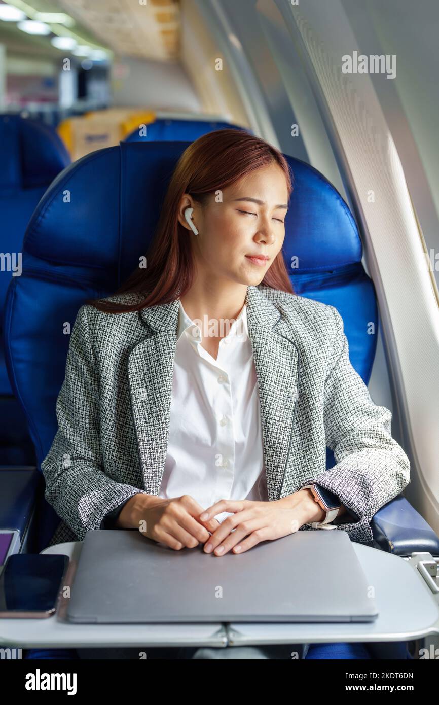 Ritratto di una donna d'affari asiatica o imprenditore di successo in un abito formale su un aereo seduto in business class. Riposo durante il volo Foto Stock