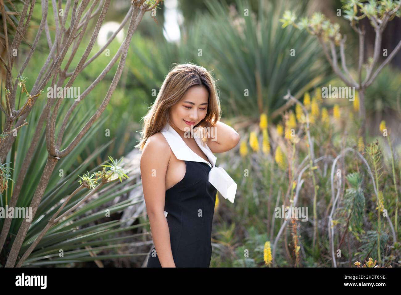 Bella giovane donna che indossa un abito corto bianco e nero in piedi in un giardino di Cactus | scena nel deserto Foto Stock