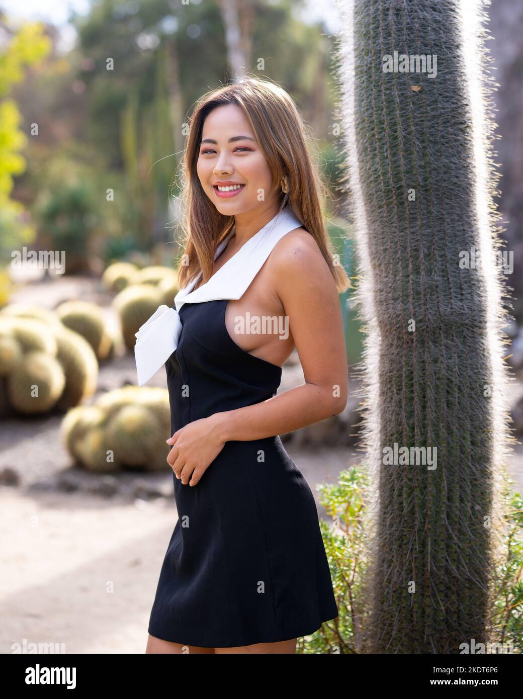 Bella giovane donna che indossa un abito corto bianco e nero in piedi in un giardino di Cactus | scena nel deserto Foto Stock