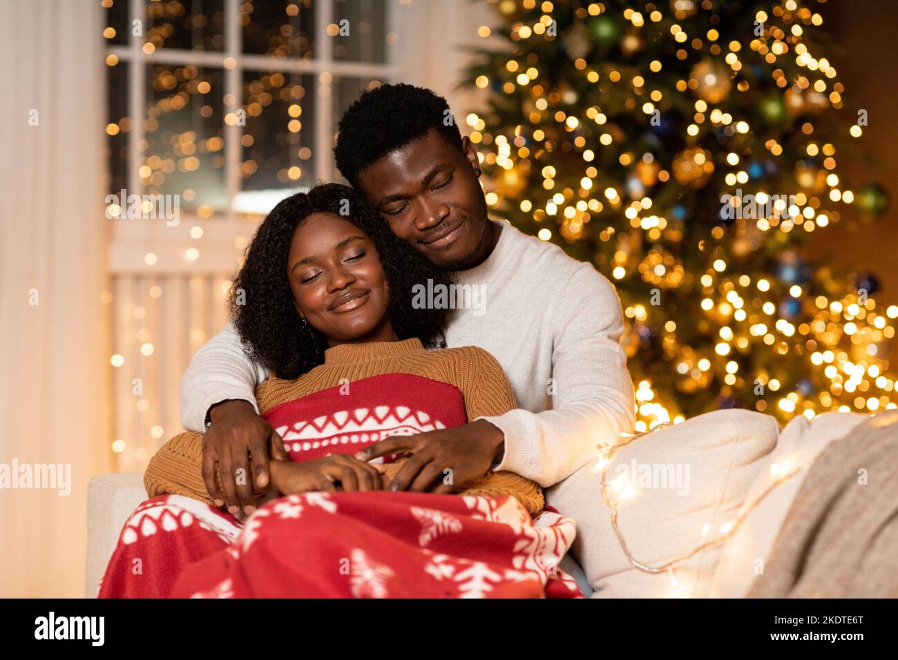 Felice uomo nero millenario abbracciando la donna con la plaid godere la vacanza, dormire insieme nel soggiorno interno Foto Stock