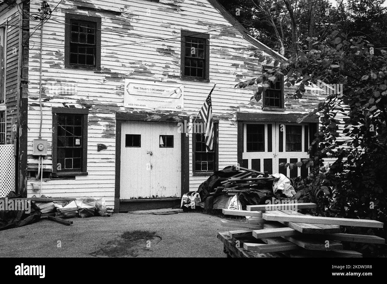 Un edificio in legno vintage indossato dalle intemperie con un cartello in tela che legge il Trusted Hammer LLC in Union, New Hampshire. L'immagine è stata acquisita in nero analogico Foto Stock