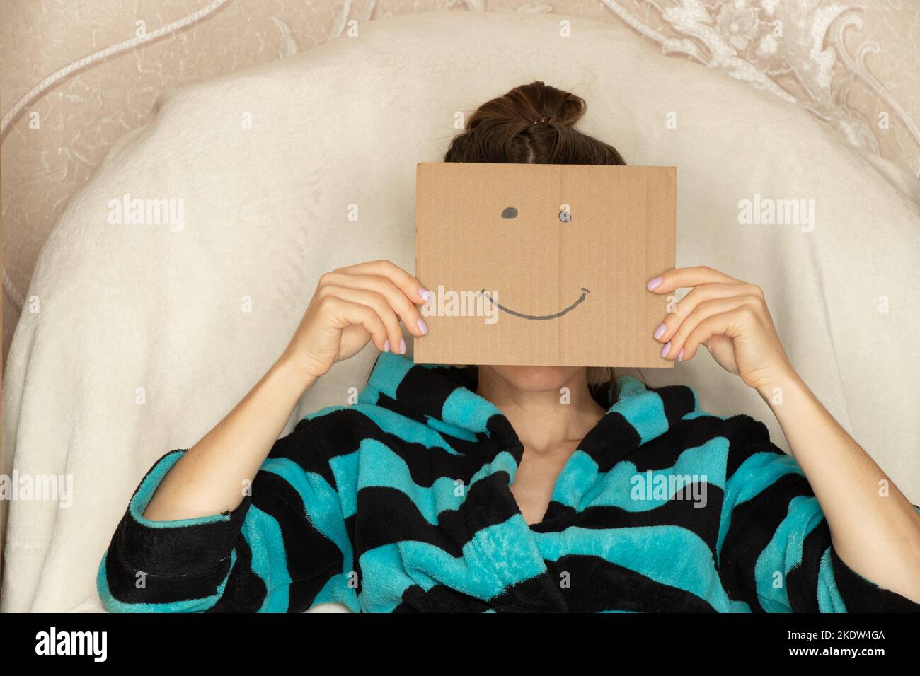 La ragazza si siede a casa in una poltrona e tiene una scatola di cartone con un sorriso allegro, buon umore e gioia Foto Stock