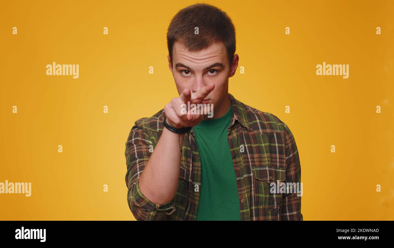 Ti sto guardando. Uomo in camicia verde casual che indica i suoi occhi e la macchina fotografica, mostra che sto guardando i gesti, spiando qualcuno. Ragazzo giovane adulto isolato da solo su sfondo giallo parete studio Foto Stock