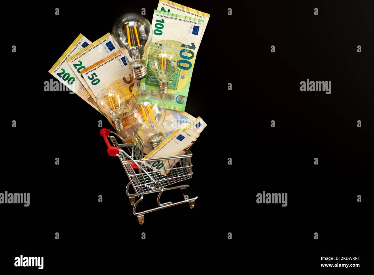 Costo dell'elettricità. Set di lampadine e banconote in euro in un carrello supermercato su sfondo nero.pagamento di bollette elettriche. Foto Stock