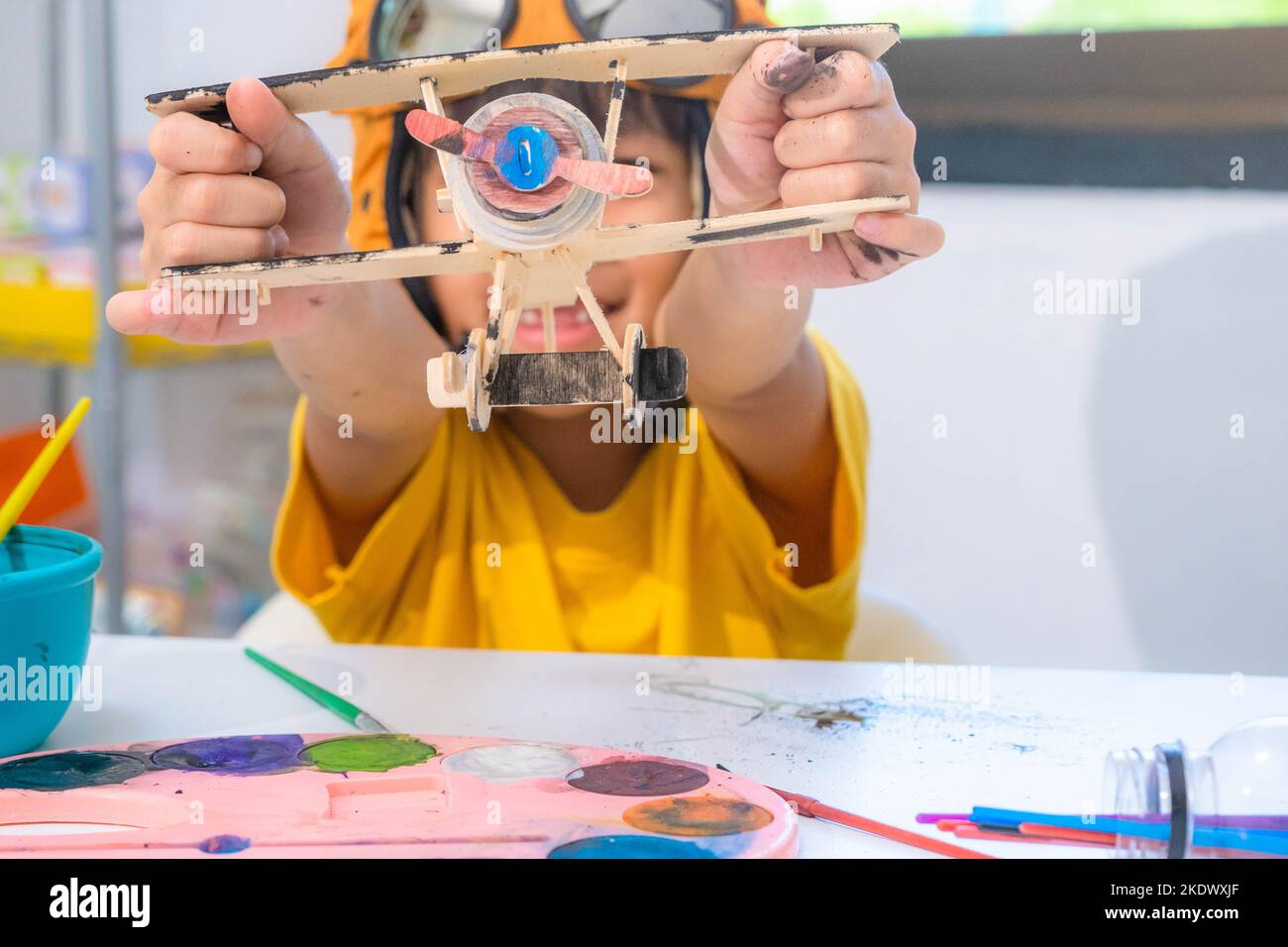 Ritratto di una felice ragazza asiatica con un pennello su un piano giocattolo di legno in classe. Arte e artigianato per bambini. Piccolo artista creativo al lavoro. Foto Stock