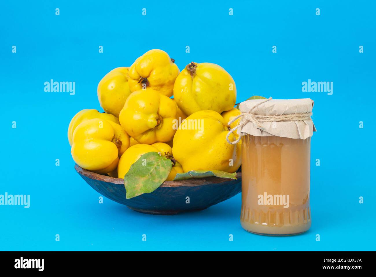 Mucchio di frutta di cotogna in una ciotola di legno, con un vasetto di marmellata senza etichetta, fuoco morbido primo piano isolato su sfondo blu Foto Stock