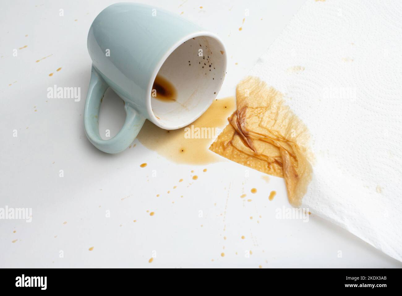 Tazza di caffè rovesciato con un velo di carta assorbente, su sfondo bianco. Primo piano con messa a fuoco morbida Foto Stock