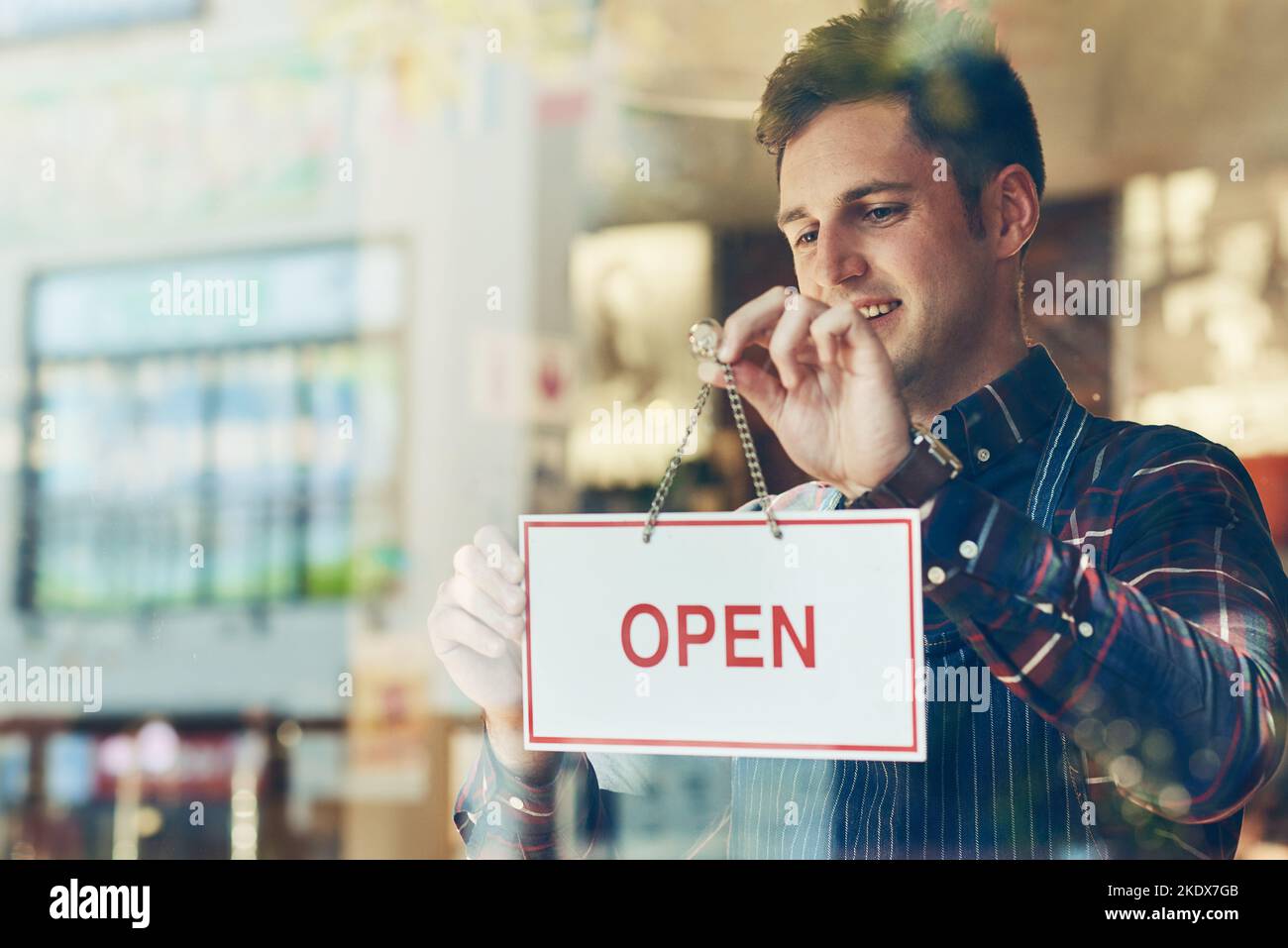 Pronto per la giornata di lavoro. Un giovane uomo che appende un cartello aperto in una vetrina. Foto Stock