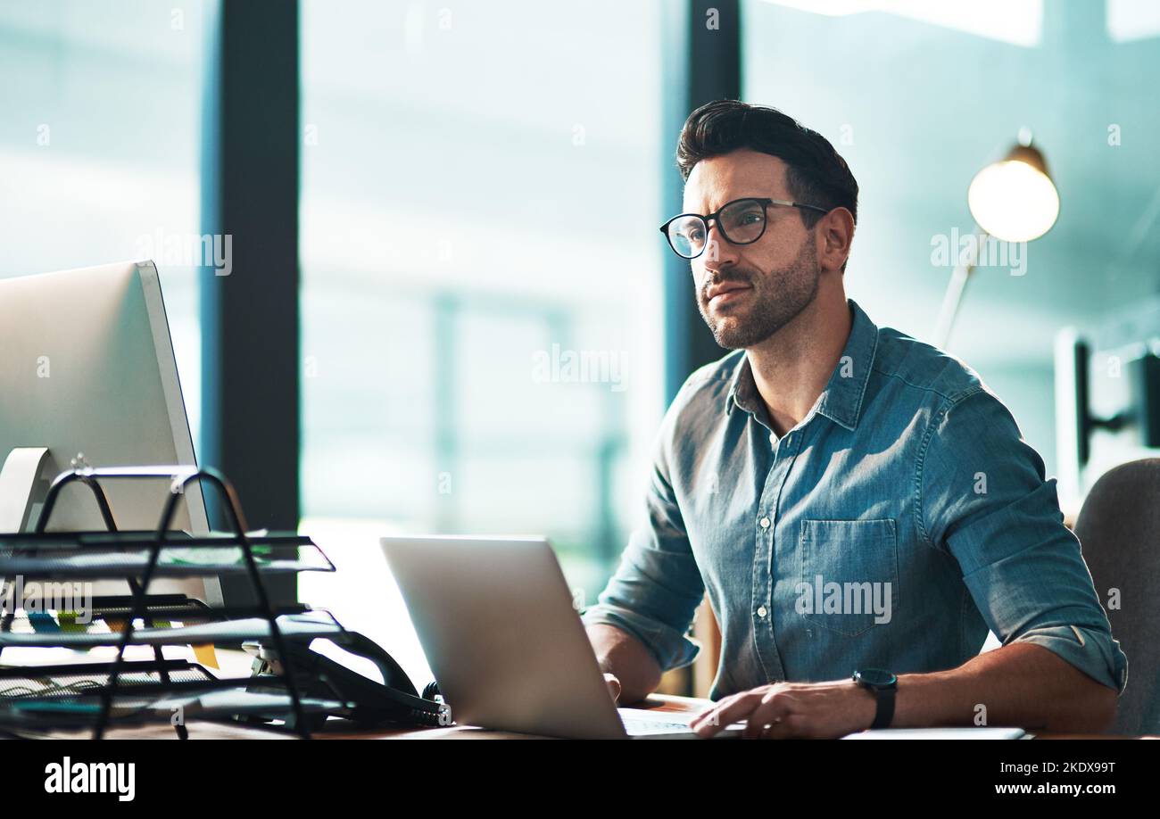 Il successo è una decisione. Un giovane uomo d'affari che guarda attento mentre usa un computer portatile alla sua scrivania. Foto Stock