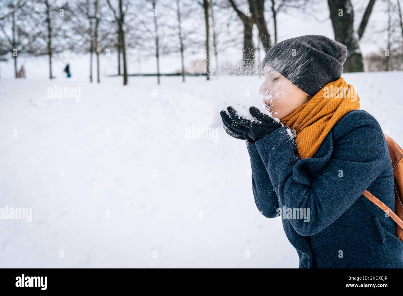 Una donna soffia la neve, raccolta nel palmo della mano sullo sfondo della natura innevata. Foto Stock