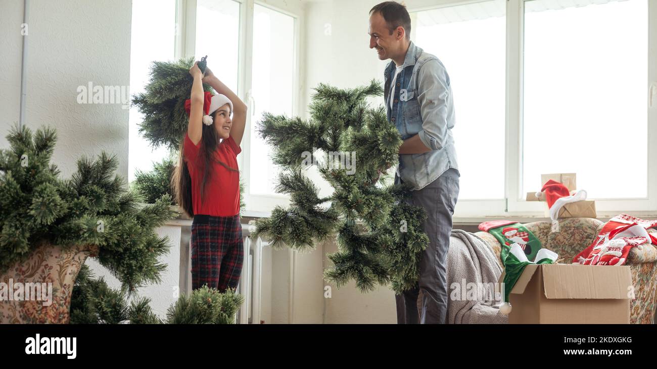 Padre e figlia che assemblano albero di natale, sorridente - natale, vacanza, concetto di inverno, attività di famiglia. Foto Stock