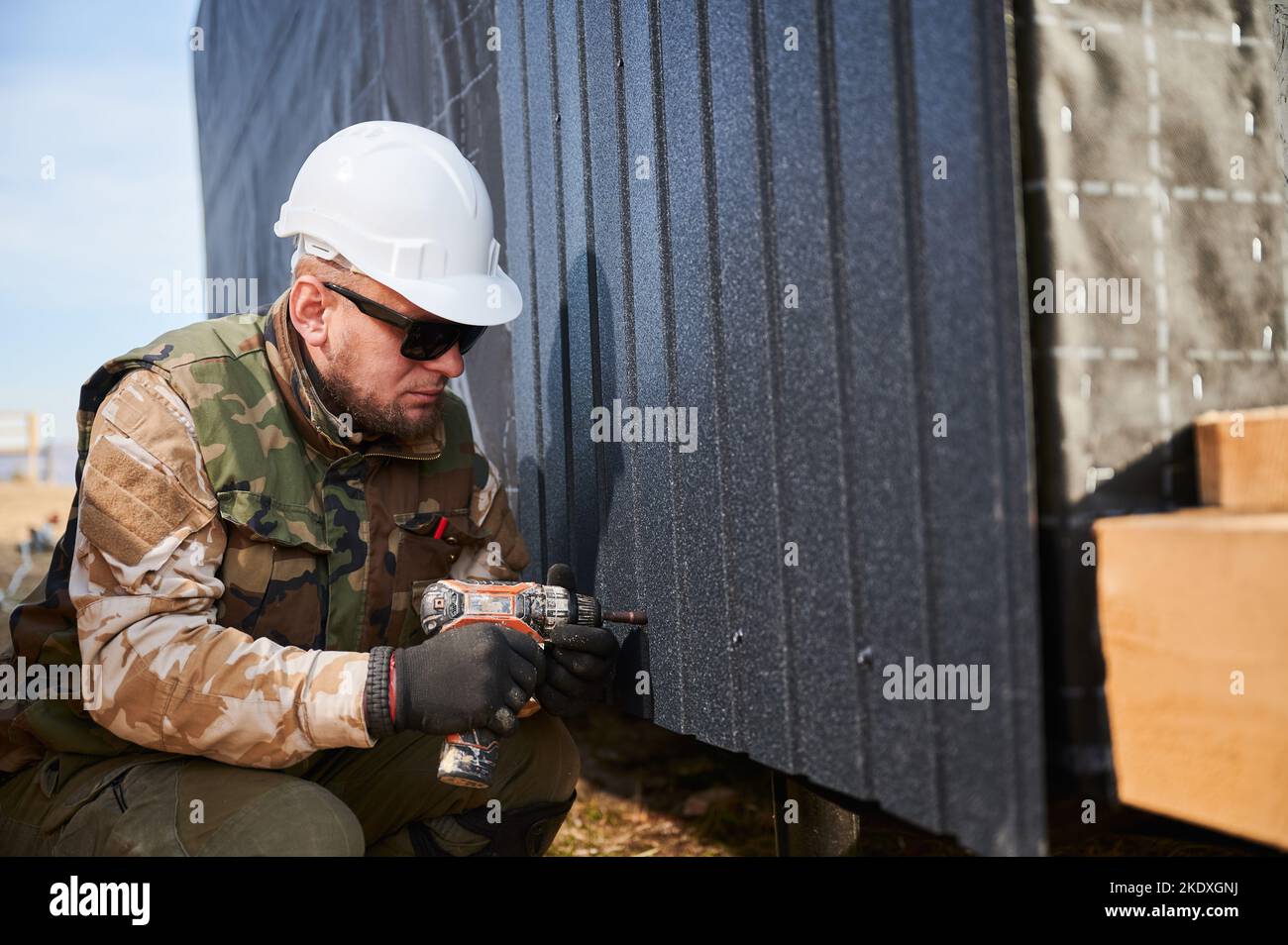Costruttore maschio che installa nero ondulato foglio di ferro usato come facciata del cottage futuro. Uomo lavoratore edificio legno telaio casa. Carpenteria e concetto di costruzione. Foto Stock