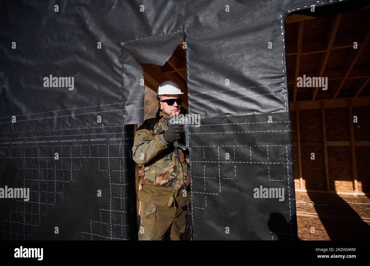 Maschio costruttore installare membrana impermeabile sul muro del futuro cottage. Uomo lavoratore edificio legno telaio casa. Carpenteria e concetto di costruzione. Foto Stock