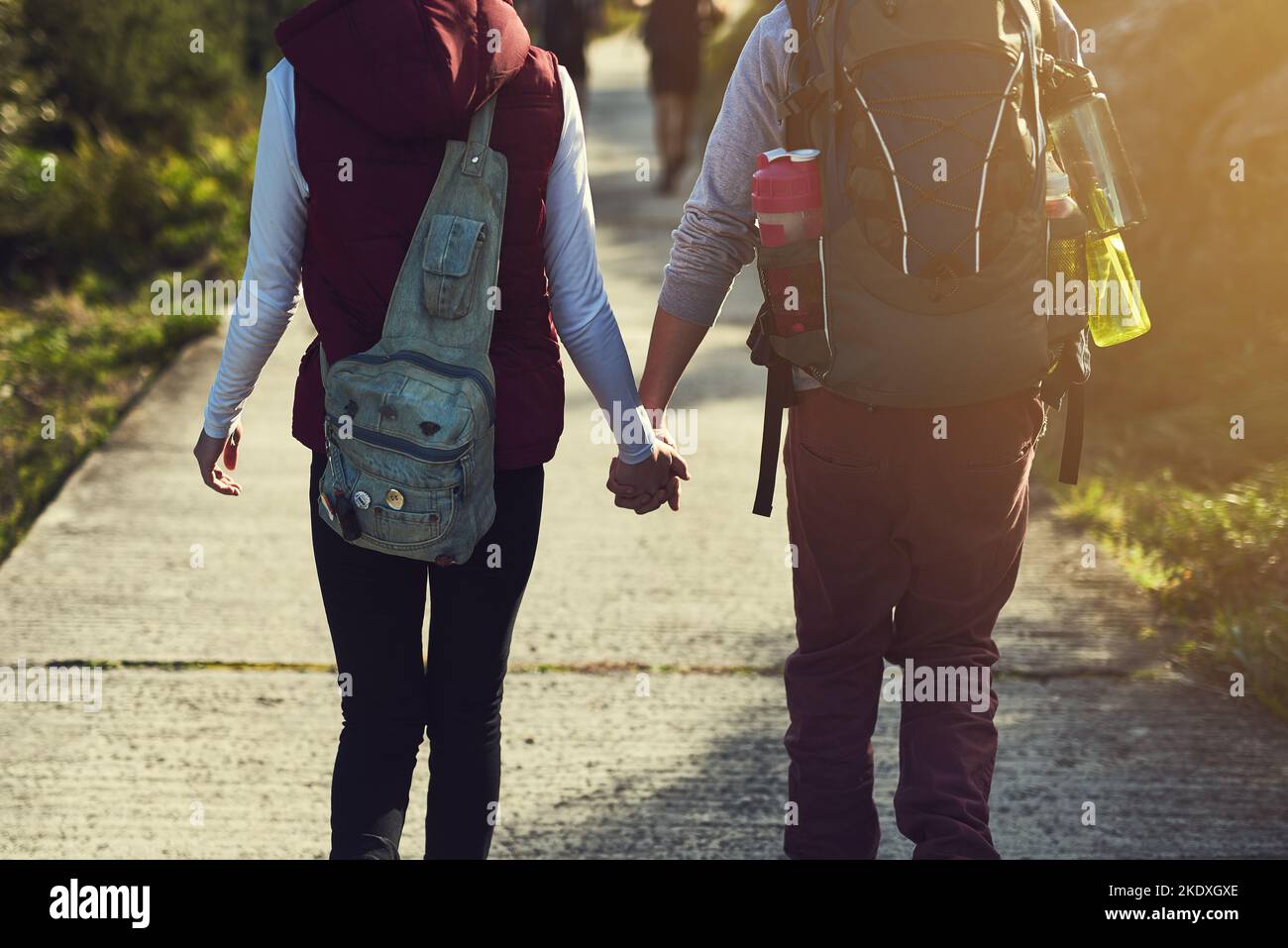 Si perde insieme. Ripresa da dietro di una giovane coppia che tiene le mani mentre cammina lungo un sentiero escursionistico. Foto Stock