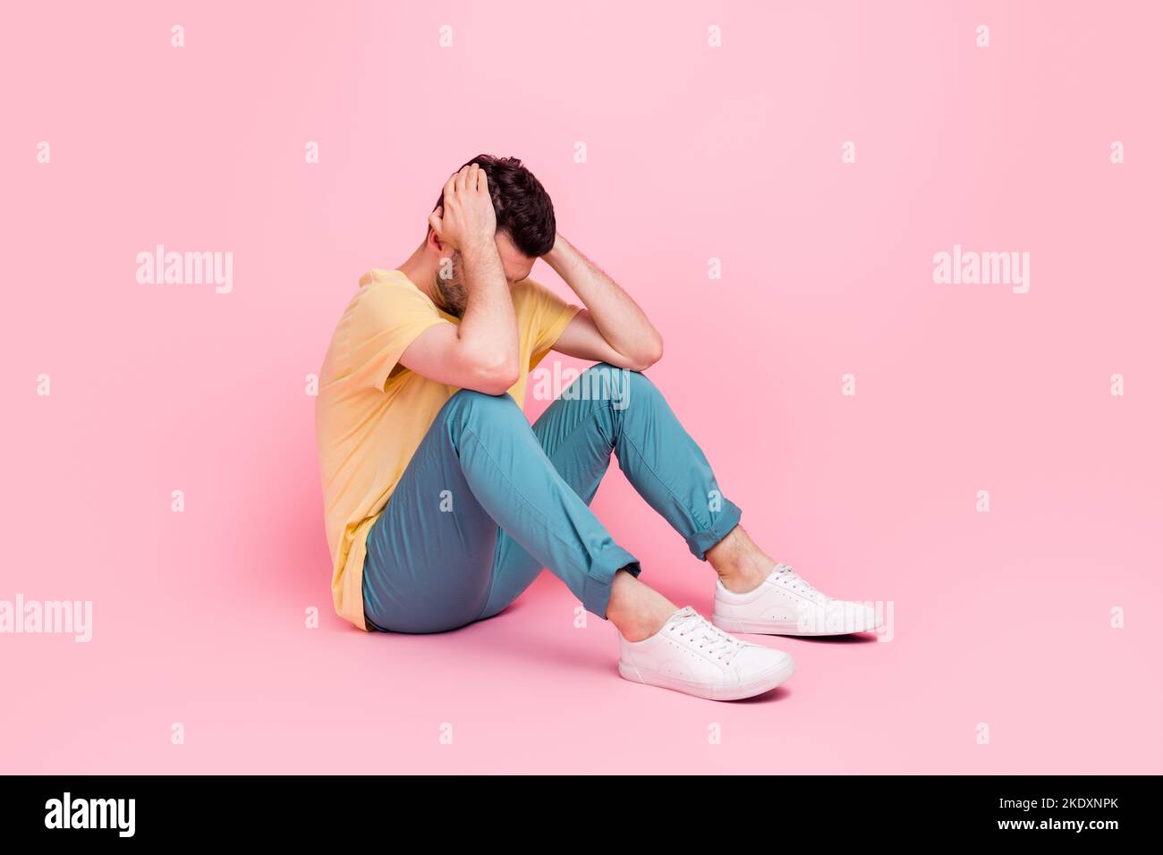 Foto di uomo triste seduta pavimento mano testa pelle faccia di copertura evitare di ignorare il mondo negativo umore isolato su sfondo di colore rosa Foto Stock