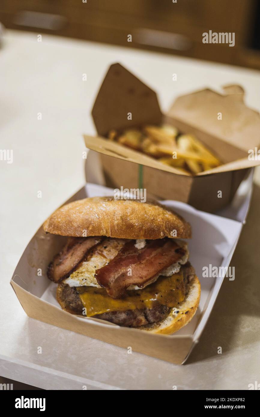 Un angolo alto di hamburger appetitoso con pancetta e fette di patate croccanti serviti sul tavolo in confezioni di cartone Foto Stock