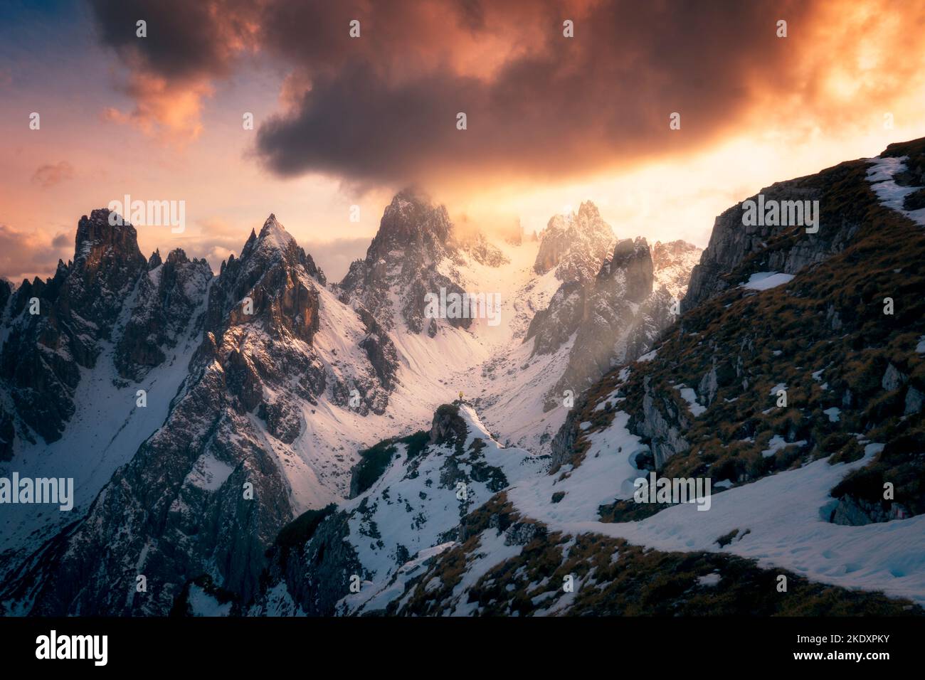 Vista posteriore del turista irriconoscibile in outerwear in piedi sulla neve e osservando tre Cime di Lavaredo cime contro cielo nuvoloso tramonto nelle Dolomiti, esso Foto Stock