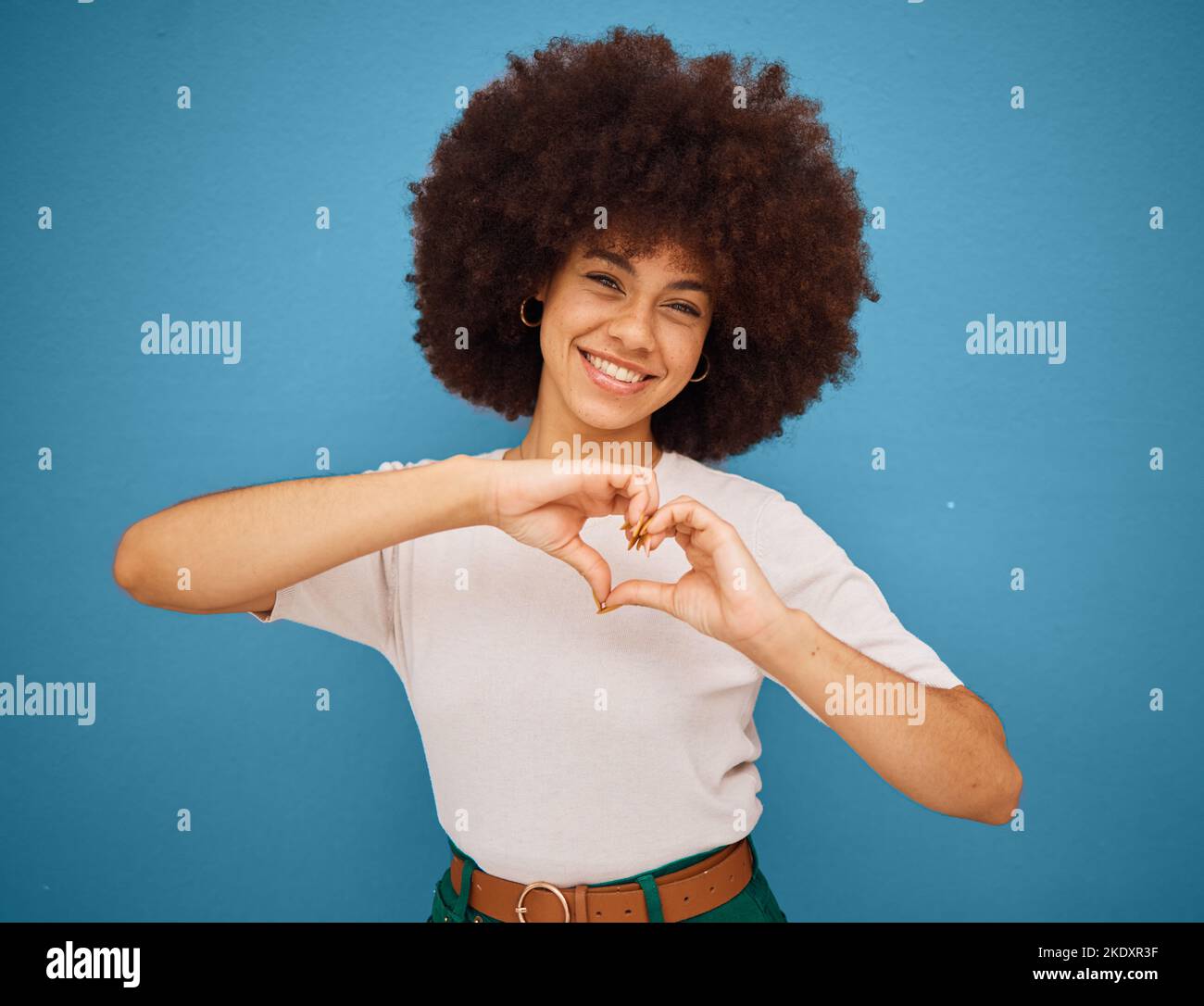 Segno di cuore emoji, mani e ragazza afro su sfondo isolato blu Foto Stock
