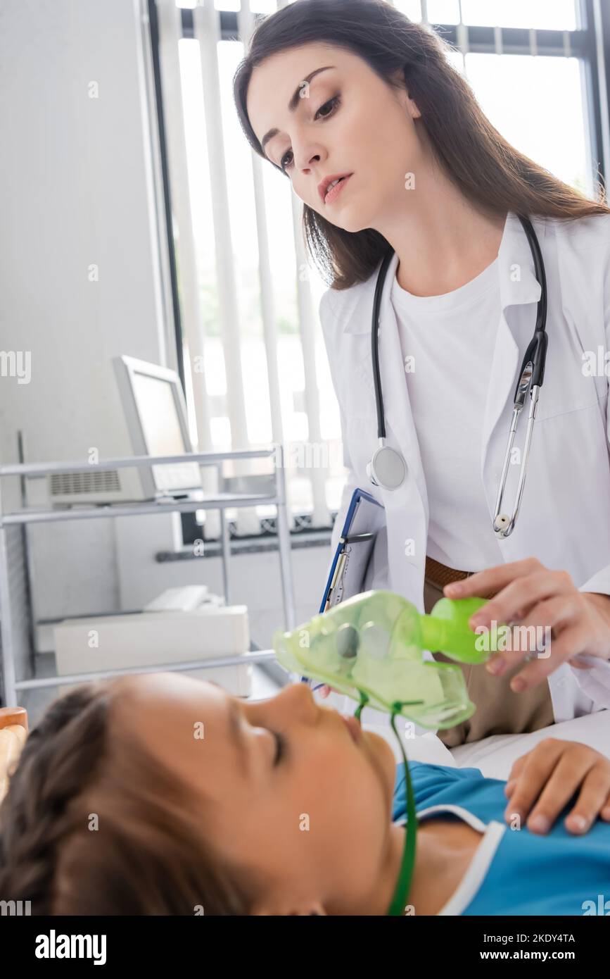 Pediatra con maschera di ossigeno e guardando il paziente in clinica, immagine stock Foto Stock