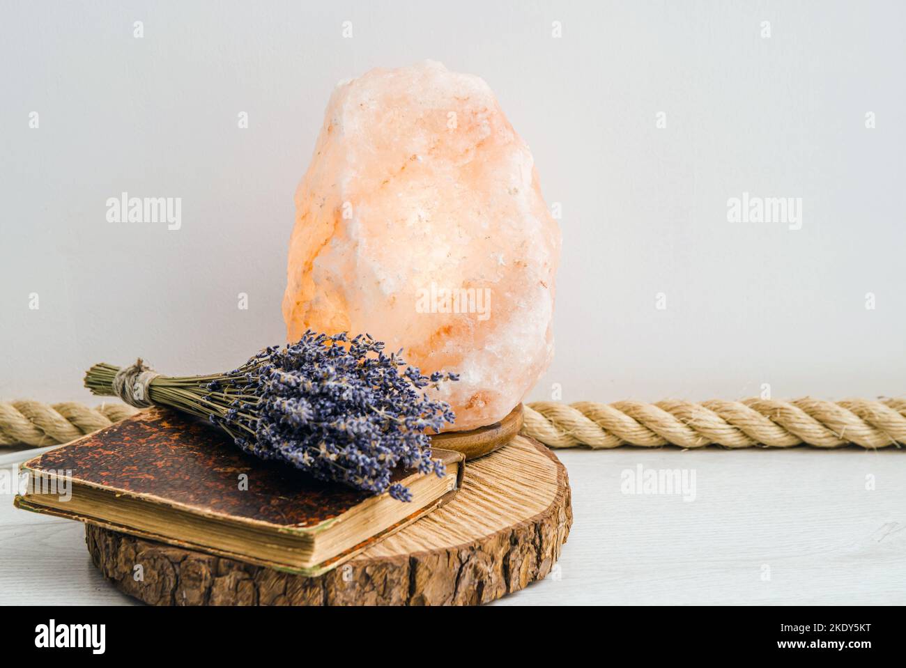 Utilizzando la fune in iuta come rivestimento del pavimento, elemento di design boho home. Pavimento bianco del soggiorno con rivestimento in corda di iuta, vassoio con disco in legno, libro d'annata e lavanda secca. Foto Stock