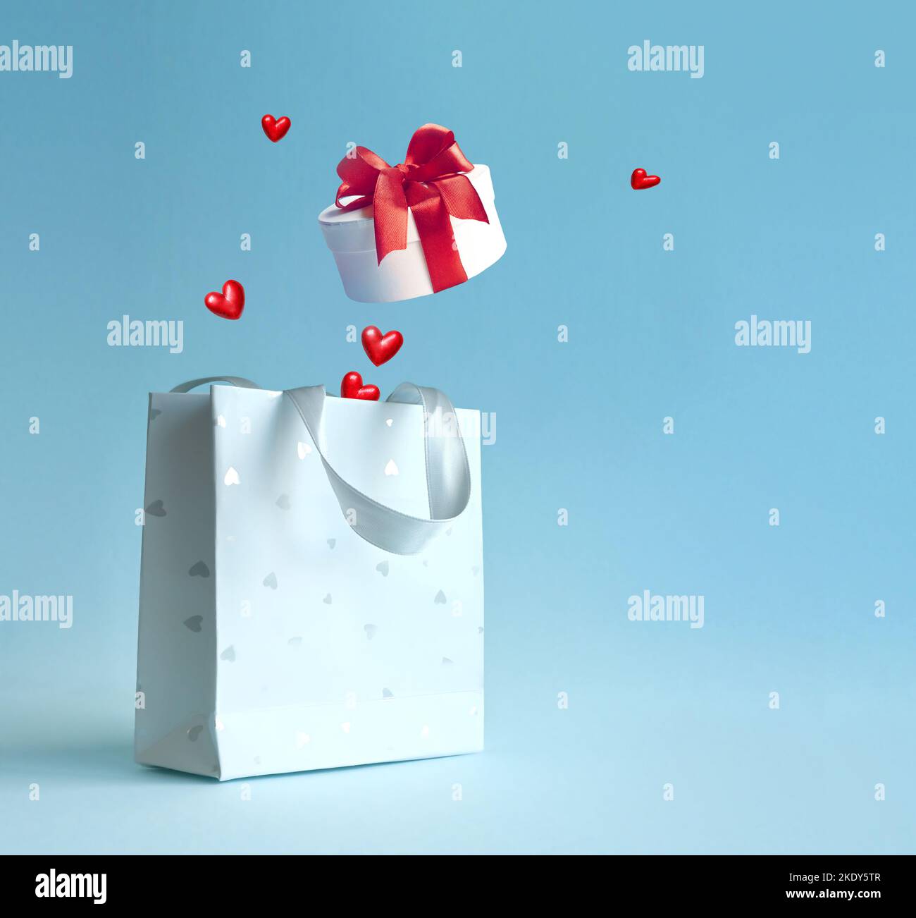 Shopping bag con scatola regalo e cuori su sfondo blu. Concetto di shopping e sconti per San Valentino Foto Stock