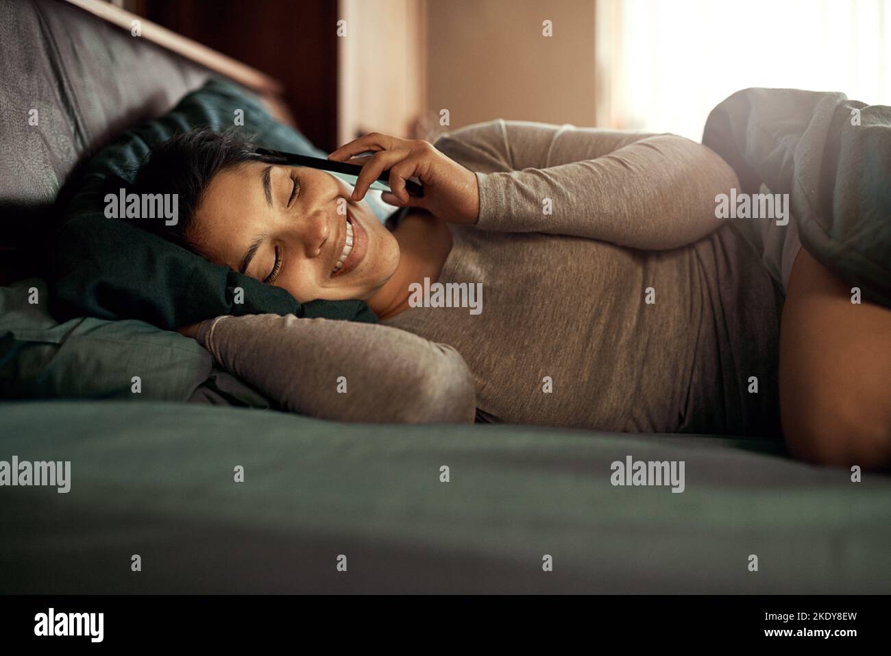 Il suo tipo preferito di sveglia telefonica. Una giovane donna felice che risponde al telefono mentre si sdraiava a letto. Foto Stock