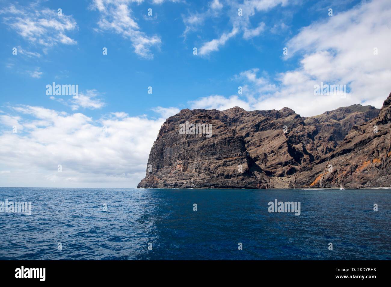Una bella vista di acque blu profonde e una scogliera rocciosa con un cielo blu chiaro e nuvole bianche Foto Stock